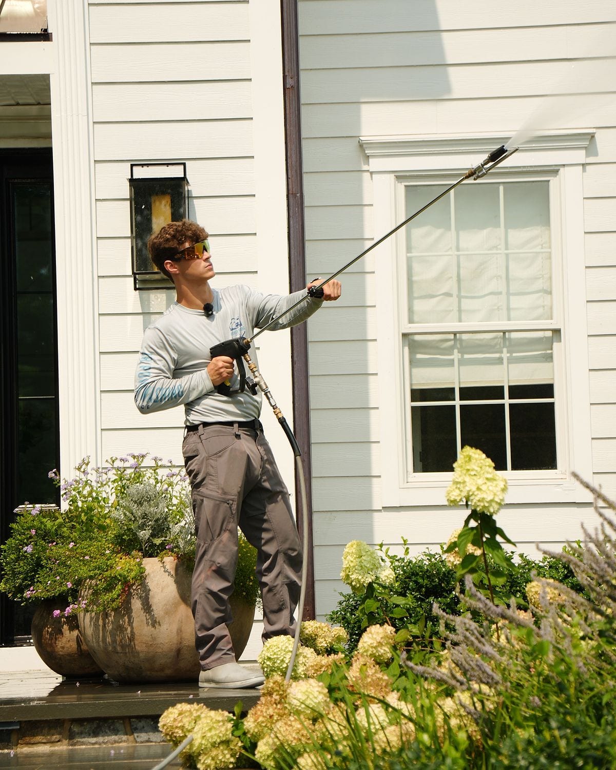 Jack Rishel, owner of JR Power Washing, soft washing the front of a home in a branded shirt